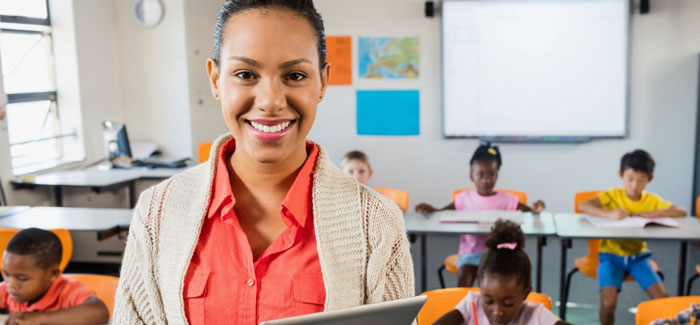 bigstock-Teacher-posing-in-front-of-cla-135884162-1180x472