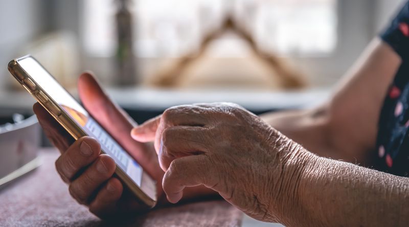 Hands of an elderly woman holding a mobile phone, close up.
